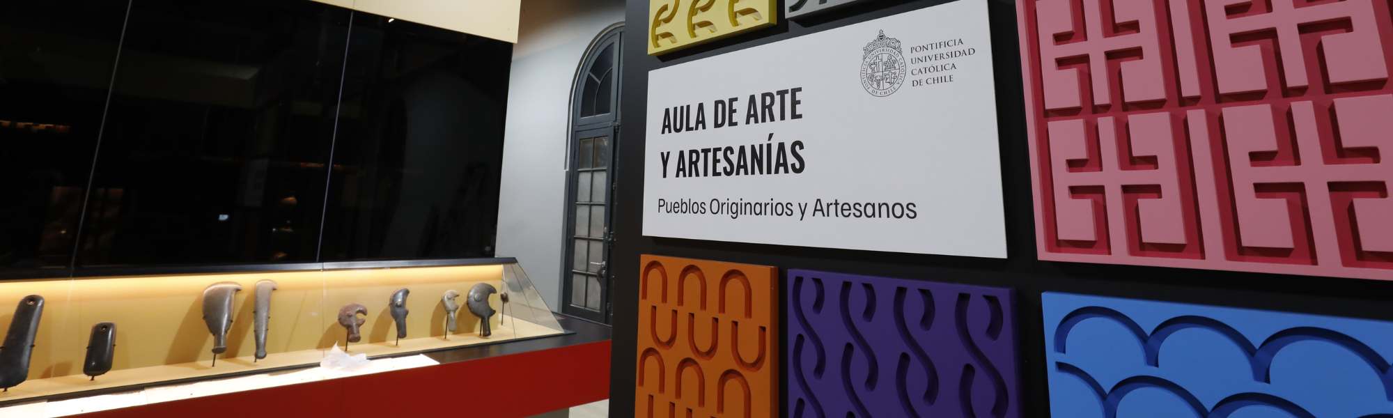 Muro con diseños coloridos y letrero señalética Aula de arte y artesanía, Pueblos originarios y artesanos